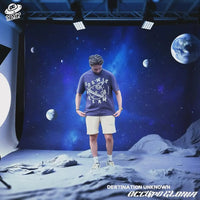 Person wearing a 'Cosmic' t-shirt on a moon-like surface with space-themed backdrop